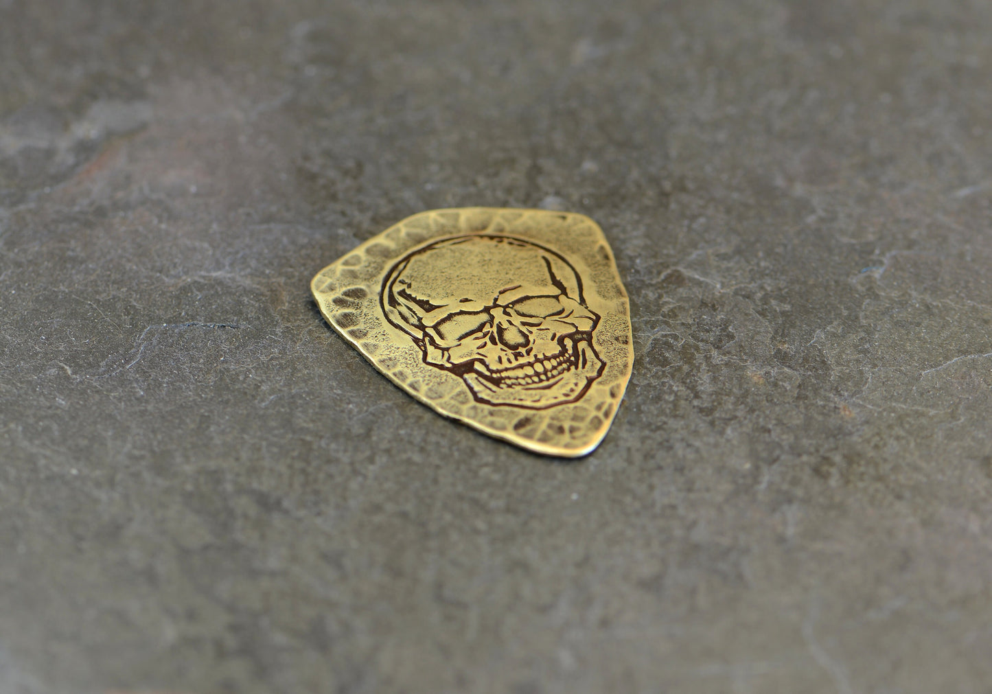 Shield style brass guitar pick with skull design