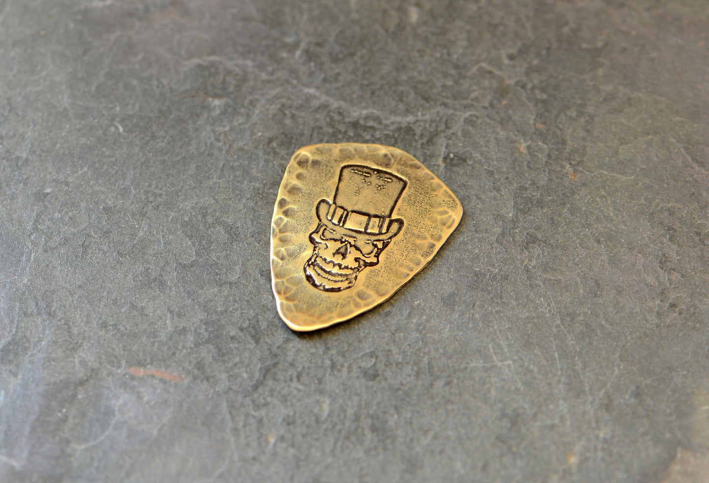 Shield shaped brass guitar pick with skull and top hat